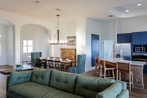 A modern kitchen with blue cabinets, a dining area with striped chairs, and a green sofa in the living room.