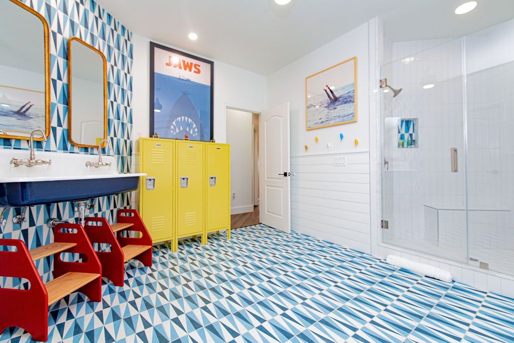 Un baño con piso de estampado geométrico, un lavamanos con espejo, taquillas amarillas y una zona de ducha.
