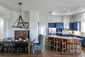 A modern kitchen with blue cabinets, a central island with bar stools, and a dining area with a wooden table and chairs.