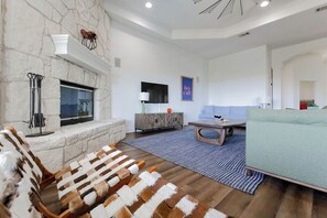 A modern living room with a stone fireplace, a flat-screen TV, a sofa, and a coffee table. - Pool/Spa | 14 Beds | Sleeps 28 - WalkerVR Sundown Escape (Austin)
