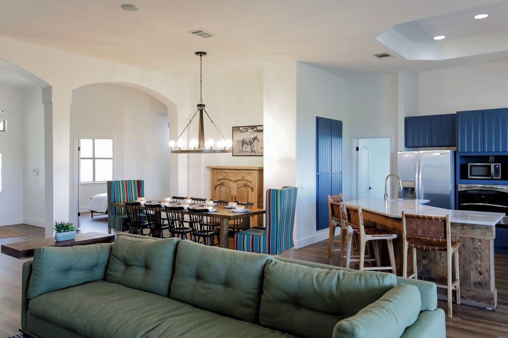 A modern kitchen with blue cabinets, a dining area with striped chairs, and a green sofa in the living room.