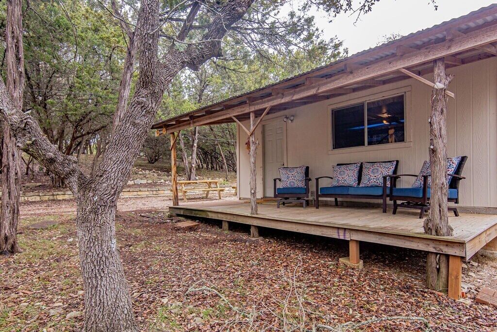 A wooden deck with a covered seating area, a window, and a view of the surrounding forest.