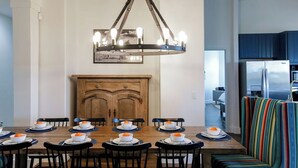 A dining area with a wooden table set for six, a chandelier, and a colorful striped chair. - Pool/Spa | 14 Beds | Sleeps 28 - WalkerVR Sundown Escape (Austin)