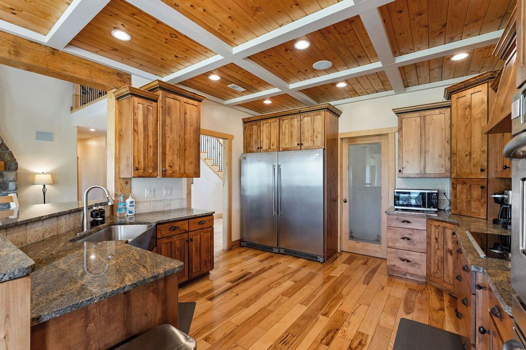 A kitchen with wooden cabinets, a stainless steel refrigerator, granite countertops, and a wooden floor.