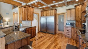 Eine Küche mit Holzausstattung, einem Edelstahlkühlschrank, Granitarbeitsplatten und Holzboden.