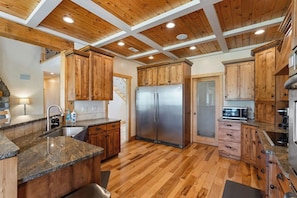 A kitchen with wooden cabinets, a stainless steel refrigerator, granite countertops, and a wooden floor.