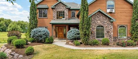 Una casa de dos pisos con fachada de piedra, revestimiento de madera y un césped bien cuidado.