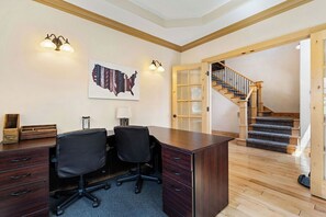 Une pièce comprenant un bureau, deux chaises, un plancher en bois, un escalier et une carte accrochée au mur.