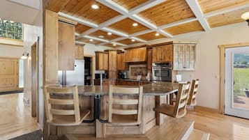 A kitchen with wooden cabinets, a central island with bar stools, and a view through a glass door.