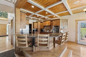 Una cocina con armarios de madera, una isla central con taburetes de bar y vistas a través de una puerta de cristal.