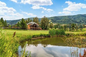 Ein Haus mit einer Holzdielen-Terrasse, umgeben von einer Wiese und einem kleinen Teich.