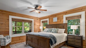 A bedroom with a wooden bed, bedside tables, a ceiling fan, and windows with blinds. - Breathtaking Views! Fast WiFi, Pool Table, Hot Tub, lvl 2 EV Charger, Fire Pit! (Maggie Valley)