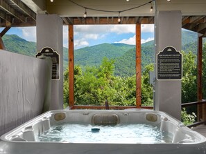 A hot tub with a view of green mountains, surrounded by wooden beams and a covered area with instructional signs. - Breathtaking Views! Fast WiFi, Pool Table, Hot Tub, lvl 2 EV Charger, Fire Pit! (Maggie Valley)