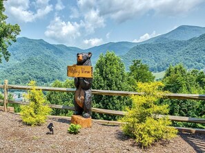 A bear statue holding a sign that reads "Valley View" with a backdrop of green hills and a wooden fence.