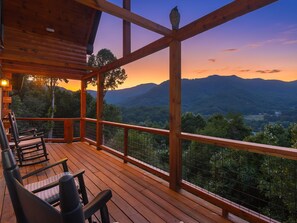 A wooden deck with chairs and a table, overlooking a mountainous landscape.