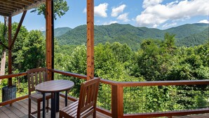 A wooden deck with a table and chairs, overlooking a forested mountain range. - Breathtaking Views! Fast WiFi, Pool Table, Hot Tub, lvl 2 EV Charger, Fire Pit! (Maggie Valley)