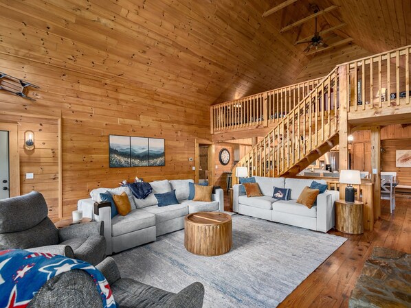 Un vaste espace de vie comprenant un grand canapé, une table basse en bois et un escalier menant à un niveau supérieur.