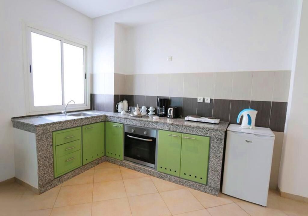 Eine Küche mit grünen Schränken, einem Backofen, einem Kühlschrank und einem Fenster.
