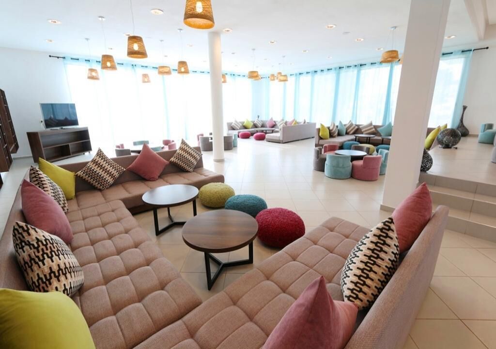 Ein großzügiger Aufenthaltsbereich mit verschiedenen Sitzgelegenheiten, darunter Sofas und runden Tischen, sowie einem Fernseher auf der linken Seite.