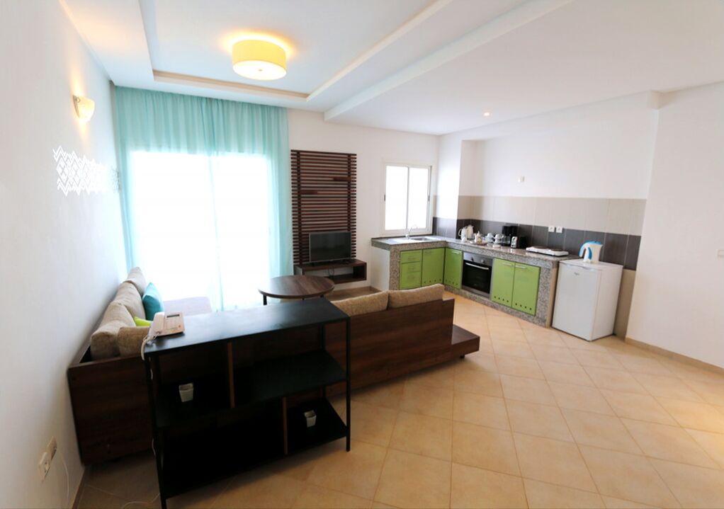 A modern kitchen with green cabinets, a white refrigerator, and a dining area with a dark wooden table and a sofa.