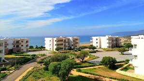 A residential area with modern apartment buildings, a parking lot, and a view of the sea.