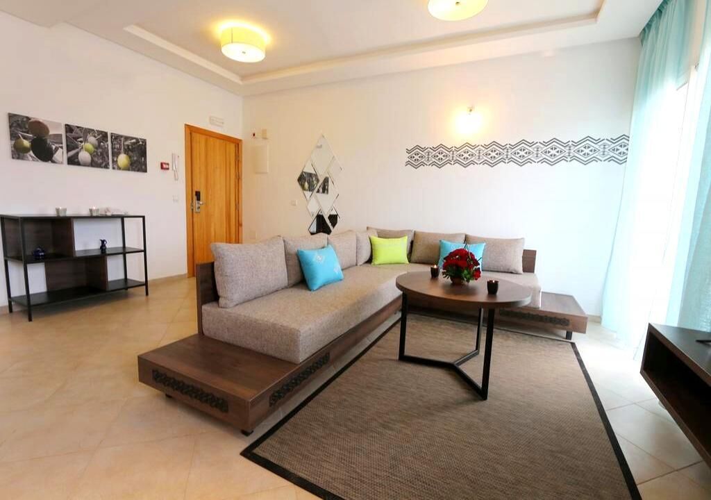 A modern living room with a sofa, coffee table, and a small side table. There is a door and a mirror on the wall.