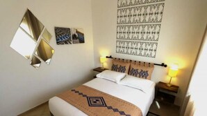 Ein Hotelzimmer mit einem Bett, zwei Nachttischen, einem Wandspiegel, Wandbildern mit Muster und einer Bettdecke mit Muster.