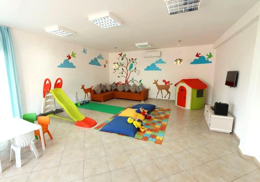 A children's playroom with a slide, play mats, and colorful wall decorations.