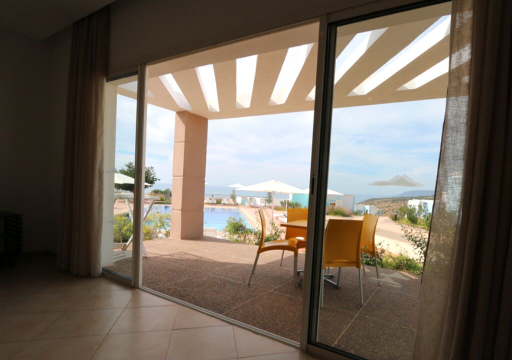 A spacious room with a large sliding glass door leading to an outdoor area with a pool, chairs, and umbrellas.