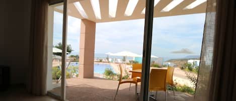 A spacious room with a large sliding glass door leading to an outdoor area with a pool, chairs, and umbrellas.