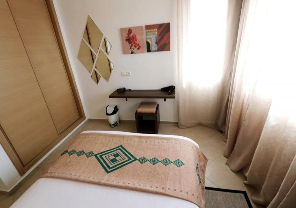 A hotel room with a bed, a desk, a chair, a wardrobe, and a small table.