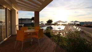 A patio with a table and chairs, overlooking a pool and a landscaped area with umbrellas.