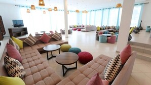 A spacious lounge area with multiple seating options, including sofas and round tables, and a television on the left.