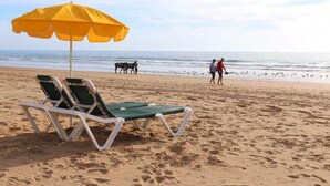 A beach with two green lounge chairs and a yellow umbrella.