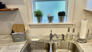 A kitchen with a double stainless steel sink, a wooden cutting board, and a metal bucket labeled 'Grove'. - Lil Gem - near Bethel and HCMC (Paris)