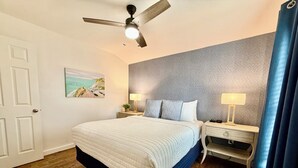 A bedroom with a bed, nightstands, a ceiling fan, a painting on the wall, and a window with curtains. - Lil Gem - near Bethel and HCMC (Paris)