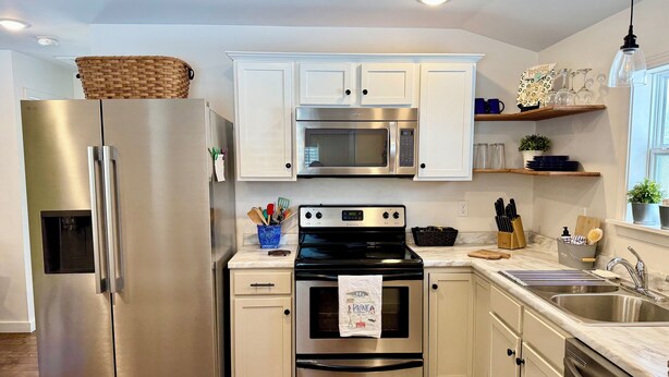 A modern kitchen with stainless steel appliances, white cabinetry, and a marble countertop. - Lil Gem - near Bethel and HCMC (Paris)