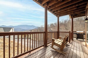 Una terraza de madera con una mecedora, una parrilla y vistas a las montañas.