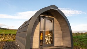 En moderne, buet bygning i træ med pod-design, glasklædt dør og et lille bord med stole indeni.