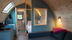Une petite cabane confortable, dotée d’une kitchenette, d’un canapé et d’un lit avec une literie à motifs floraux.
