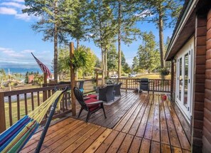 A wooden deck with outdoor furniture, a hammock, and a view of the ocean. - Cabin near Flathead Lake is walking distance to food, shopping and lake view. (Lakeside)