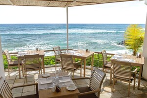 Un restaurante frente al mar con mesas y sillas de madera, numeradas para los comensales.