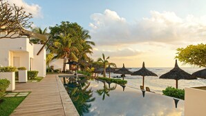 Zona de piscina tranquil·la amb un tramat de fusta, palmeres i paraigües de palla que donen a l'oceà.