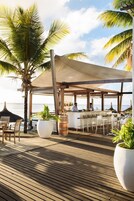 Una terraza de madera con mobiliario exterior, una zona de bar y palmeras.