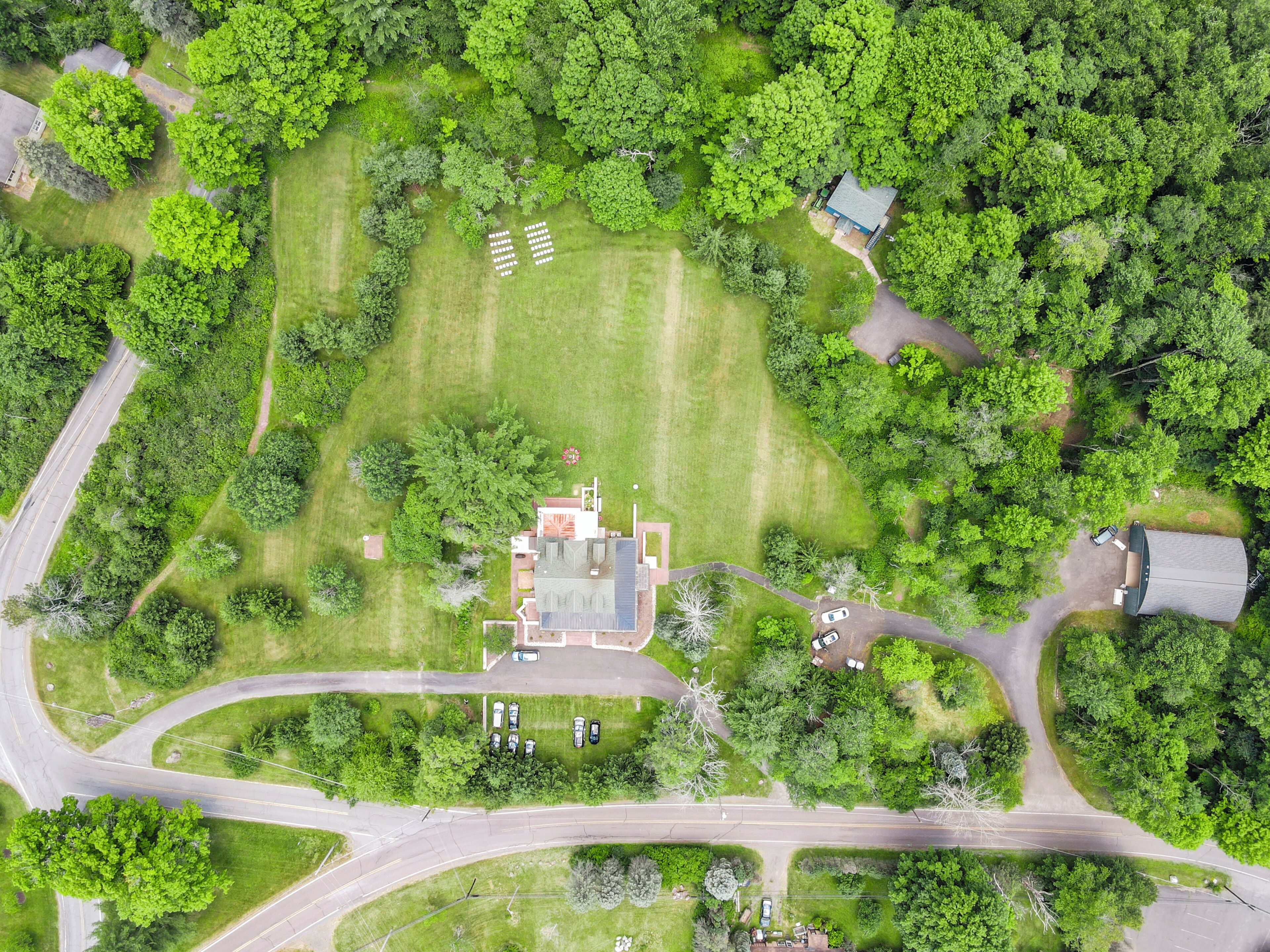 A residential area with a central house surrounded by lush greenery, a driveway, and a curved road.