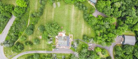 A residential area with a central house surrounded by lush greenery, a driveway, and a curved road.