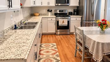 A modern kitchen with white cabinets, stainless steel appliances, a granite countertop, and a dining area with a table and chairs.