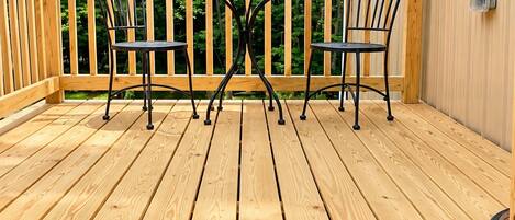 Una terraza de madera con una mesa y sillas de metal, rodeada por una barandilla de madera.