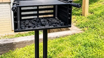 A barbecue grill with charcoal on a stand in front of a building.