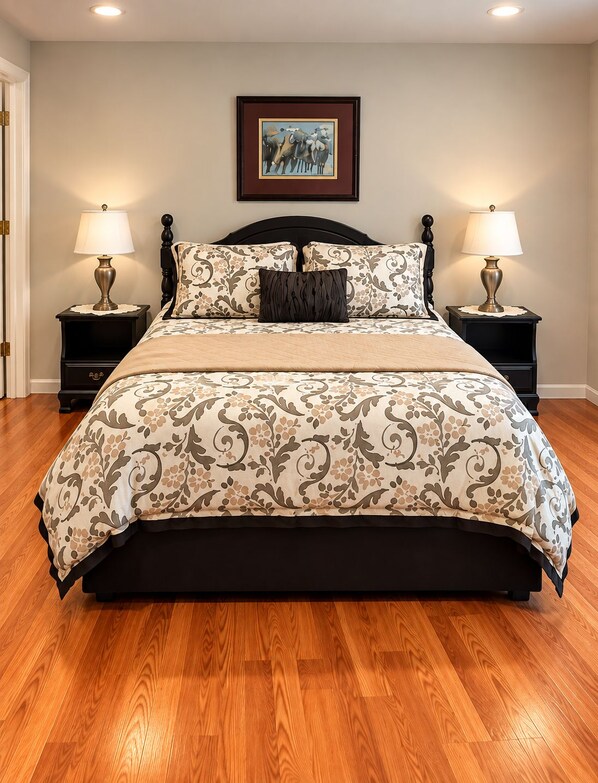 A bedroom with a large bed, two bedside tables with lamps, a framed picture on the wall, and wooden flooring.